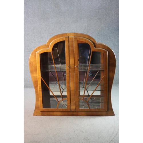 41 - An Art Deco walnut cloud shaped display cabinet with sunray astragal glazed doors on plinth base. H.... 