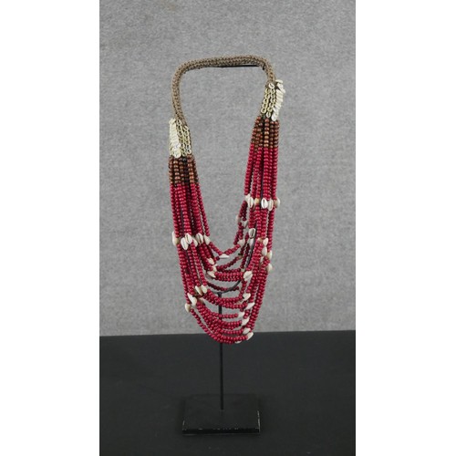4 - A tribal wooden bead and cowrie shell multi stranded necklace on metal display stand. H.56 W.12 D.12... 