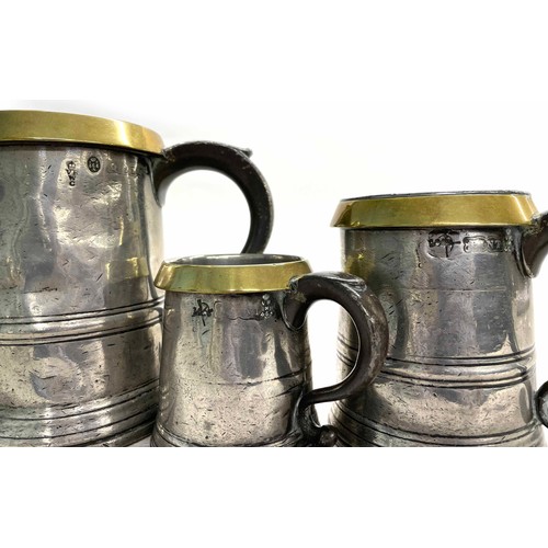 21 - Three early 19th century pewter tankards to include a quart, pint and half pint, each with brass rim... 