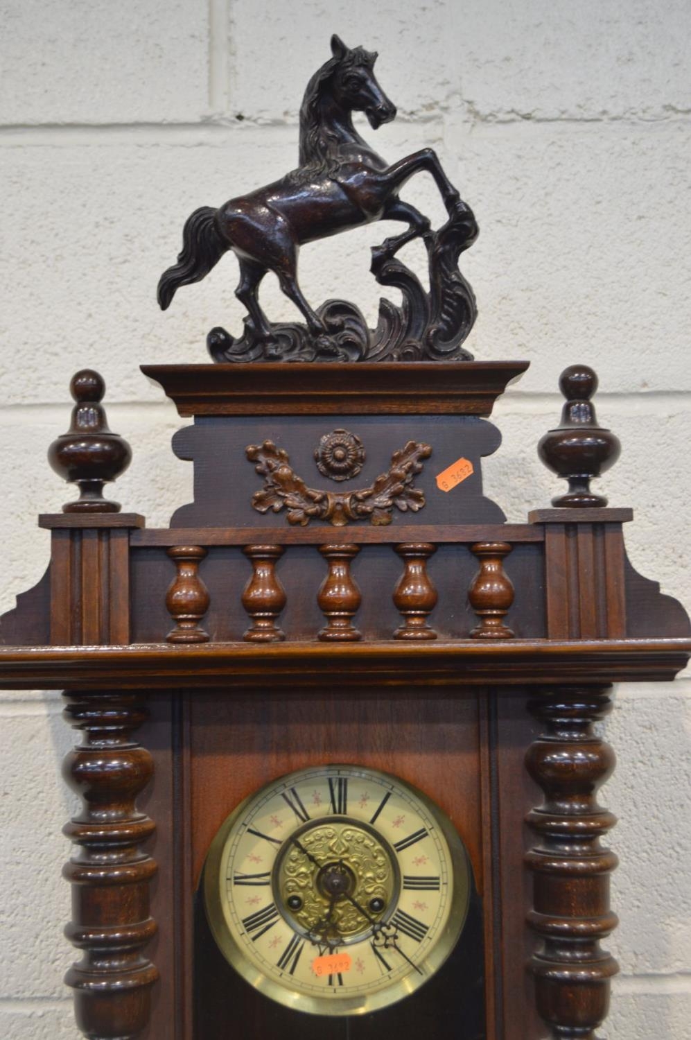 A MAHOGANY VIENNA WALL CLOCK, with a ceramic horse pediment, various turned finals, the door enclosi