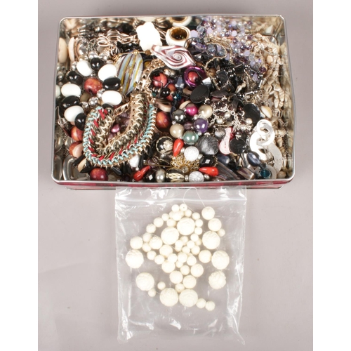 25 - A tin of costume jewellery. Including beads, necklaces, etc