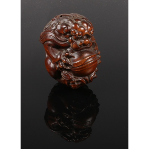 An extensively carved boxwood netsuke, formed as  temple lion holding a ball. Length 6cm.