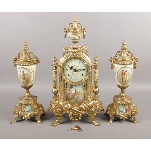 A gilt metal Lancini three piece clock garniture, with porcelain panels depicting figures and scenes to the base and main body. The clock itself is supported by two ceramic pillars, with a twin handled urn to the top; each piece topped with fruit. Height: 42cm.