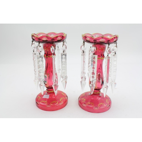 72 - A pair of cranberry gilt decorated trumpet shaped lustres, hung with faceted drops.