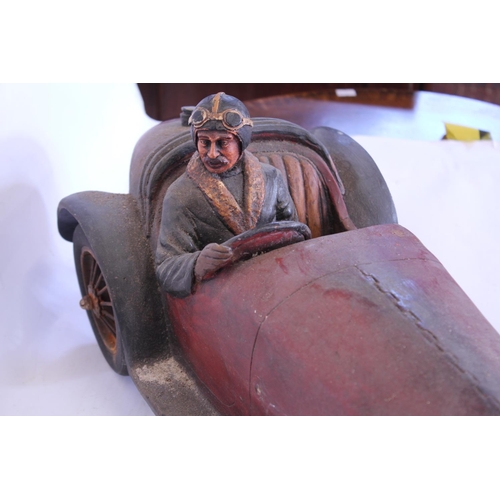 666 - A Resin model of a Racing Driver in a Race Car. Measuring: 60cms long. (AF).