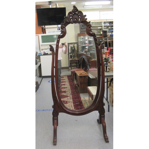 1 - A late Victorian/Edwardian mahogany framed cheval mirror, the oval plate within an ornately carved f... 