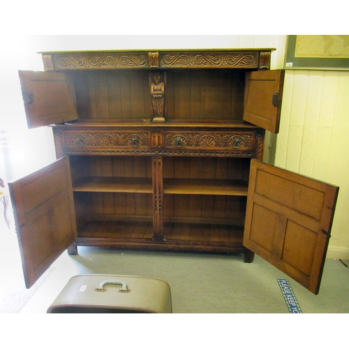 50 - A 1920s/30s carved oak court cupboard, the frieze drawer over a pair of recessed doors and outset fl... 