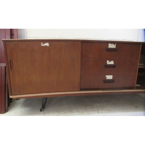 35 - A 1970s teak sideboard with a sliding door, a central bank of three drawers and two open shelves, ra... 