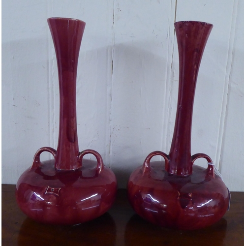 36 - A pair of streaky red glazed pottery vases, each with a tall, slender neck, twin handles and a bulbo... 
