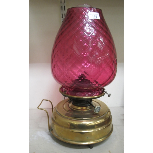 58 - An early 20thC oil lamp with a cranberry coloured glass shade and a clear glass funnel, over a brass... 