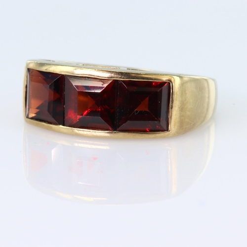 31 - 9ct yellow gold band ring set with three princess cut garnets measuring approx. 6mm x 6mm in a chann... 