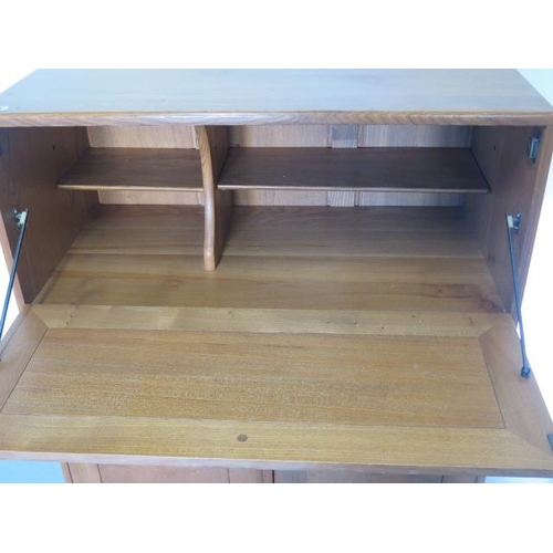 20 - An Ercol light elm cabinet with a drop front above two cupboard doors above a drawer on casters, 110... 