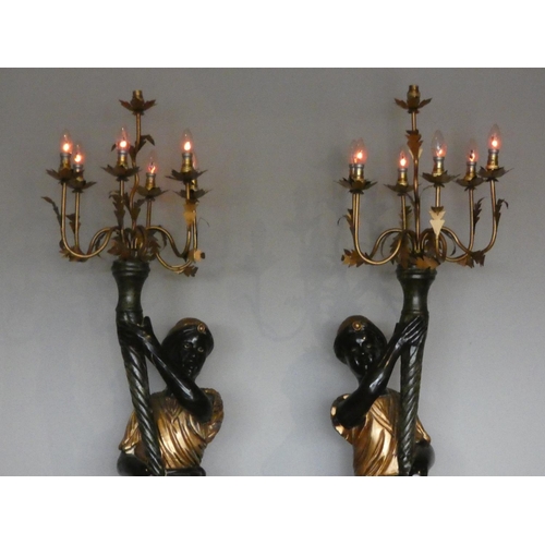 387 - A pair of painted wood Blackamoor standard lamps, in black and gold, supporting seven light chandeli... 
