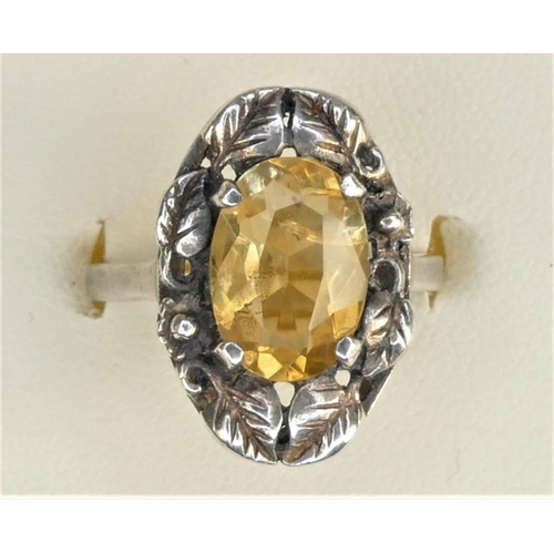 131 - An Arts & Crafts silver and citrine ring, calw set with a mixed cut stone, floral frame, size L 1/2.