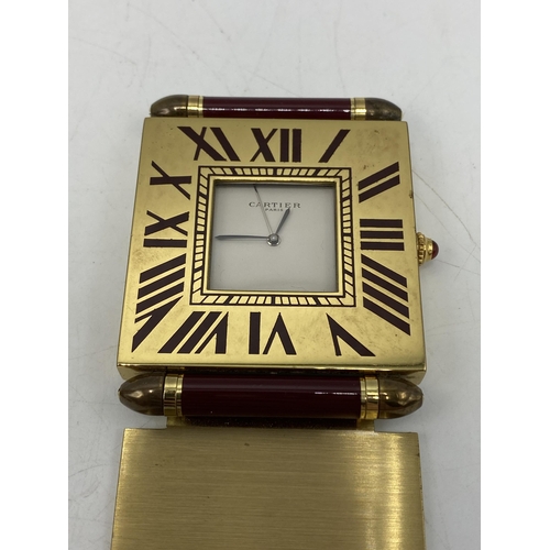 51 - A Cartier quartz folding bedside/travel alarm clock having a white dial in a brass case with burgund... 