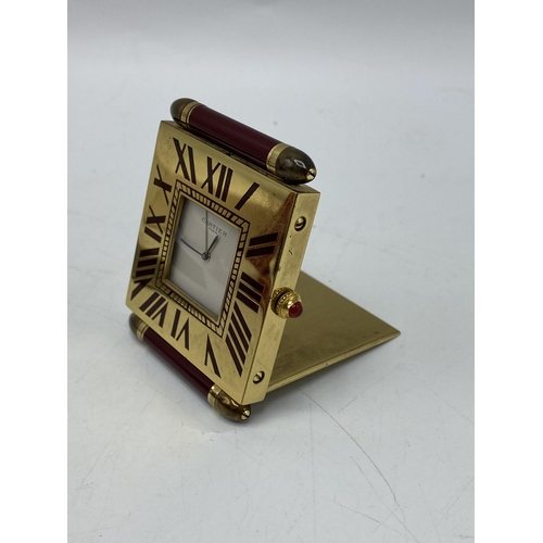 51 - A Cartier quartz folding bedside/travel alarm clock having a white dial in a brass case with burgund... 