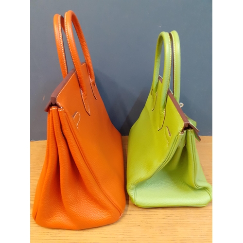 2 - Two modern leather handbags in the style of the Birkin bag, one in orange and the other in lime gree... 