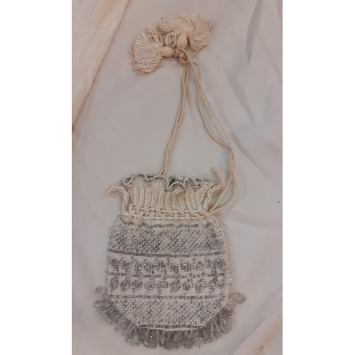 13 - An early 20th Century cream knitted evening bag with silver coloured beadwork and tasselled fastenin... 