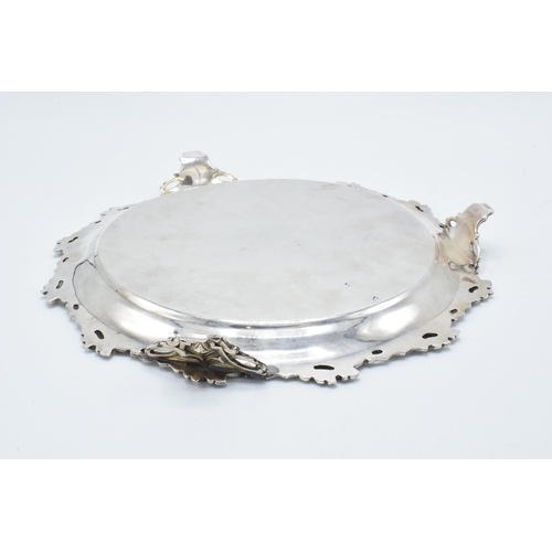 210O - A large silver plated salver raised on three ornate feet with unusual decoration. 26cm wide.