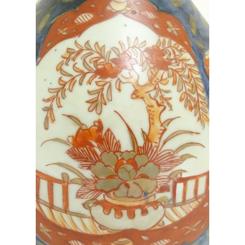 35 - An Oriental double gourd vase in the Imari palette with lobed panels depicting plants on a terrace, ... 