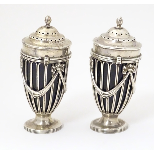 274 - A pair of silver pepperettes of urn shape with bow and swag detail and blue glass liners. Hallmarked... 
