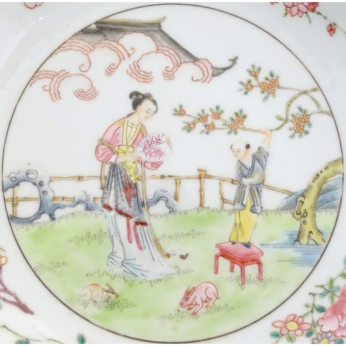 19 - A Chinese famille rose plate decorated with a woman holding a fan in a garden terrace with a young a... 