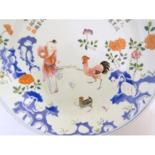 21 - A Chinese famille rose plate decorated with a figure, a cockerel, hen and chicks in a garden with fl... 