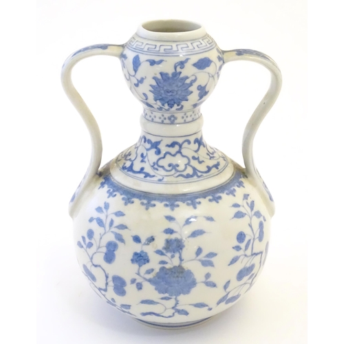 24 - An Oriental blue and white double gourd vase with twin handles decorated with scrolling floral and f... 