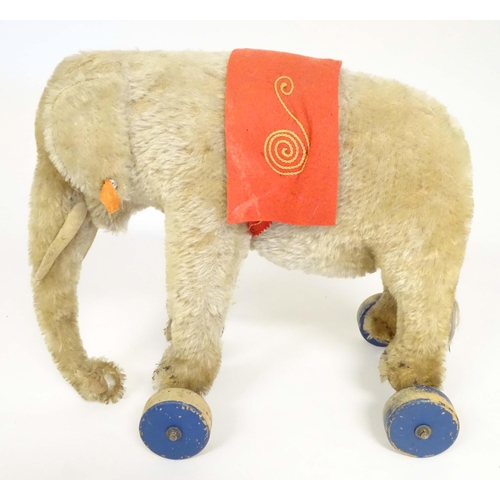 1373 - Toy: An early 20thC Steiff mohair pull along elephant toy with felt saddle, upon four wooden wheels,... 