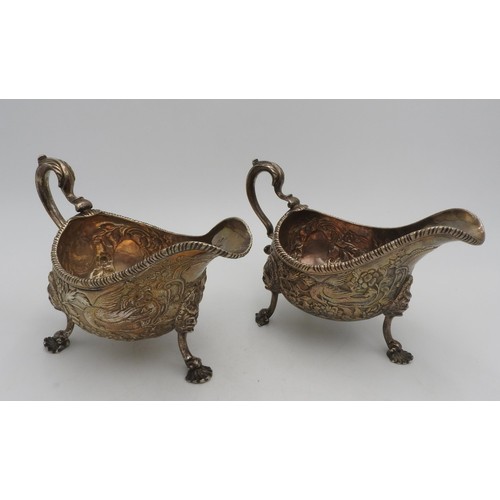 A PAIR OF LARGE IRISH HALLMARK SILVER SAUCEBOATS, with extensive foliate and bird embossed decoration, ornate scroll work handles, on three legs with portrait panels and shell feet, one sauceboat bears a heavily rubbed harp hall mark and indistinguishable hallmark, the other a heavily rubbed crown hall mark, 21 cm spout to handle, 15cm high, total weight for the pair 35 oz