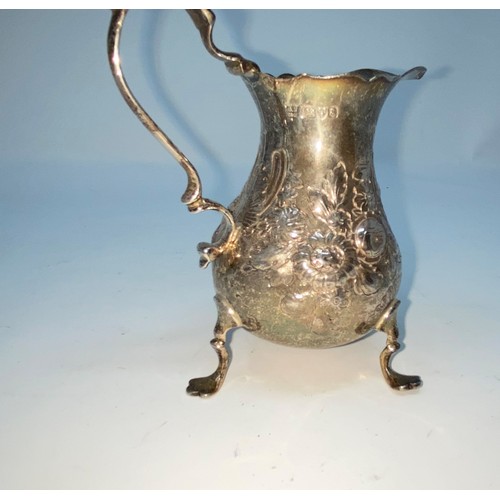 414A - A hall marked silver milk jug with relief decoration of flowers on three raised feet Chester 3.8oz