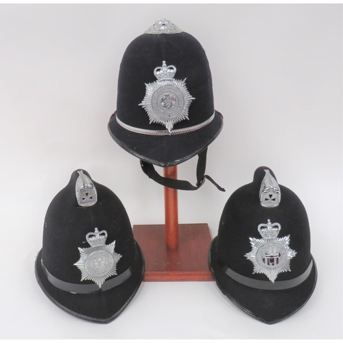 Three Post 1953 Police Officer Helmets
consisting dark blue covered crown, front peak and rear brim.  Top chrome rosette.  Chrome, QC North Yorkshire Police helmet plate.  Webbing chinstrap.  Together with similar example with top comb with front chrome mount.  Chrome, QC Derbyshire Constabulary helmet plate ... Similar example with chrome, QC Northumbria Police helmet plate.  Some service wear and minor damage.  3 items.