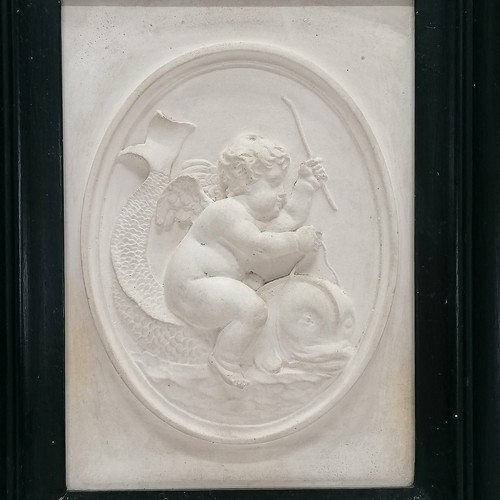 566 - Ebonised framed plaster relief / panel depicting a cherub riding a dolphin - 26cm x 31cm