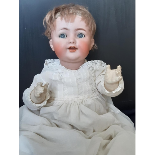 Bisque head 'Dolly faced' doll by Kammer & Rheinhardt (head by Simon & Halbig), early 20th century, with 5 piece bent limb composition body, blue flirty eyes, and open mouth with teeth. Doll is dressed in a long white gown, with a woollen undergarment of similar length and knitted underwear. Height 45cm. Head needs re-stringing