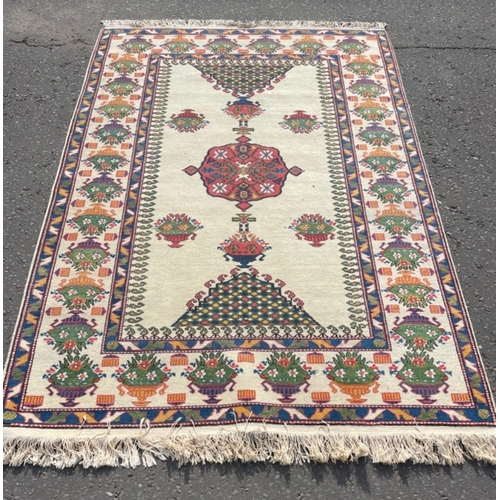 142 - A VINTAGE HANDMADE TRADITIONAL INDIAN CARPET with a creamy coloured background with urns of floral d... 