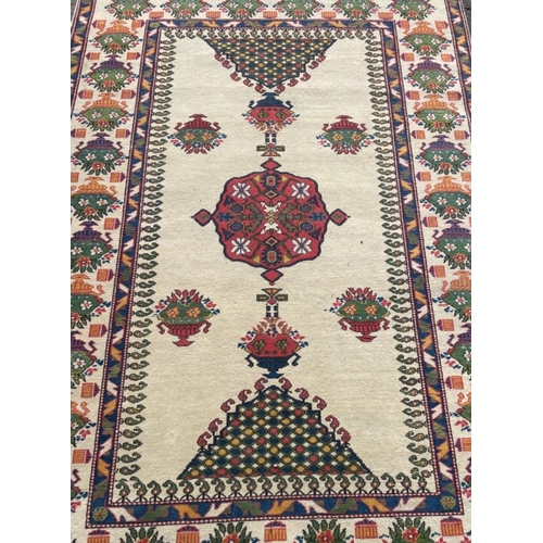 142 - A VINTAGE HANDMADE TRADITIONAL INDIAN CARPET with a creamy coloured background with urns of floral d... 