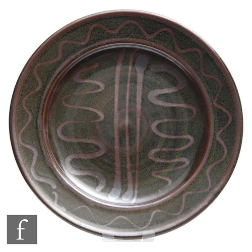 11 - A Winchcombe Pottery dish decorated with brown wavy and straight lines in an oxide glaze against a s... 