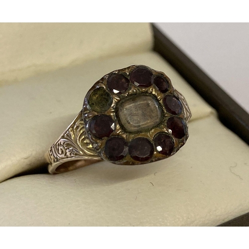 18 - A Georgian gold mourning ring with central  glass panel surrounded by round cut garnets, 1 missing. ... 