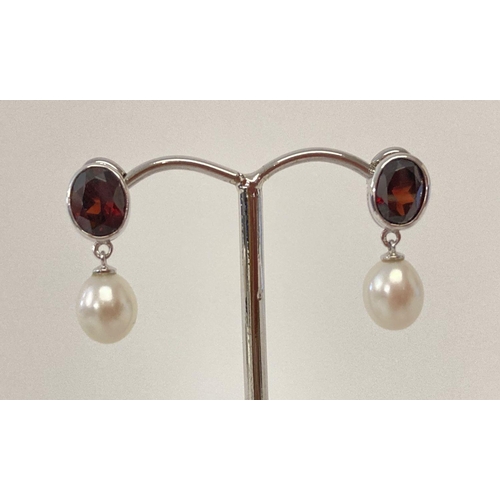 1015 - A pair of 9ct white gold, garnet and pearl drop style earrings. Each earring has a bezel set oval cu... 