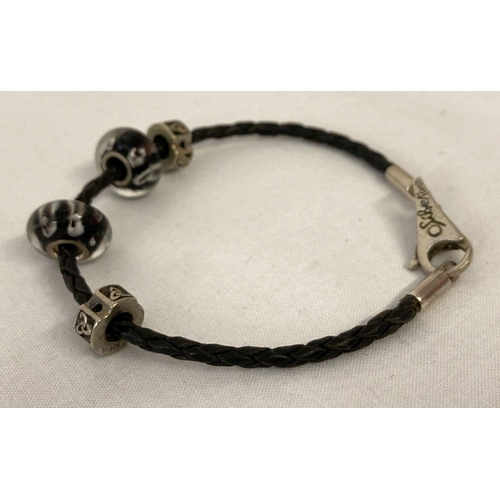 1032 - A silver and black plaited leather bracelet by Silverado, together with 4 charm beads. Makers name a... 