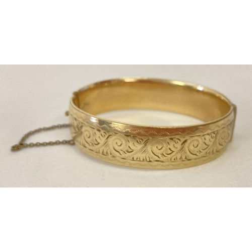 1047 - A vintage 9ct gold with metal core hinged bangle with half floral decoration and safety chain. With ... 