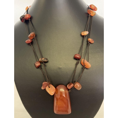 1057 - A modern design cord and carnelian necklace. A large central piece of polished carnelian with smalle... 