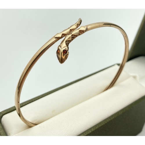 1003 - A 9ct gold thin bangle with snakes head & tail detail set with small garnet stones. Approx. 6.5cm di... 