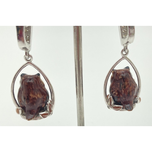 1057 - A pair of silver enamelled brown owl and flower detail drop style earrings. Small clear stones set t... 