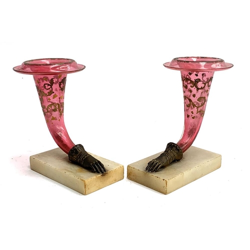 A pair of cranberry glass cornucopias with brass hand terminals, with painted foliate decoration, each on alabaster plinth, 20cmH