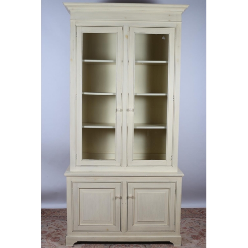 16 - A CREAM PAINTED CABINET the moulded cornice above a pair of glazed doors containing adjustable shelv... 