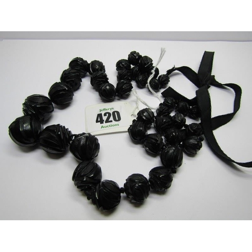 420 - A STRING OF CARVED GRADUATED JET BEADS; On black cord with ribbon tie
