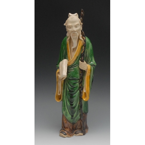 25 - A Chinese figure, of  an elder, he stands holding a stick and scroll, green robe with yellow edges, ... 