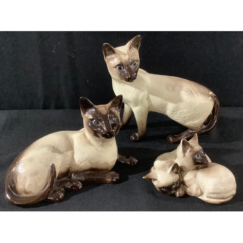 18 - A Beswick model of a Siamese cat, standing; another, recumbent; a model of two kittens (3)