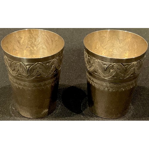 43 - A pair of possibly low grade silver tapering cylindrical tots, chased and engraved, 5cm, marks indis... 